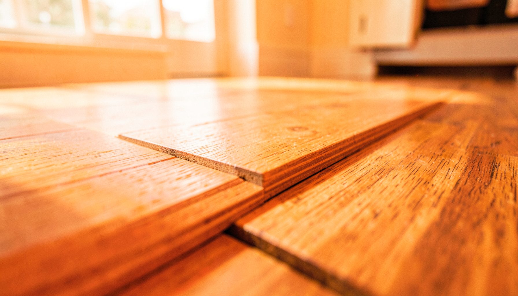 A close-up of interlocking wood-plastic composite flooring planks in warm oak tones, laid across a bright interior room with soft natural light.